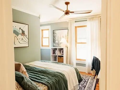 Cozy bedroom with green walls, large windows, and contemporary decor featuring a ceiling fan.