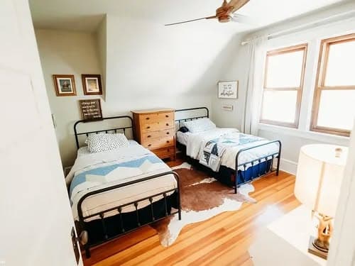 Cozy bedroom with two twin beds, wooden dresser, and natural light from windows.