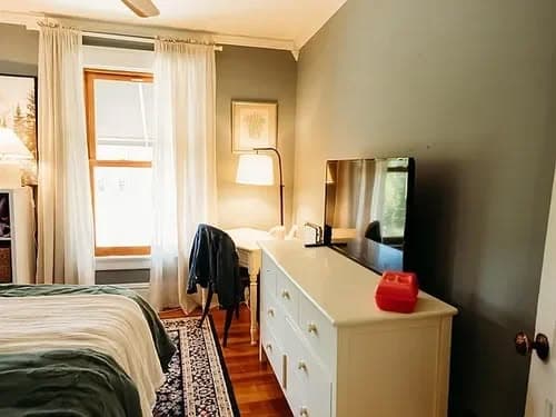 Cozy bedroom with a white dresser, television, and natural light through window.