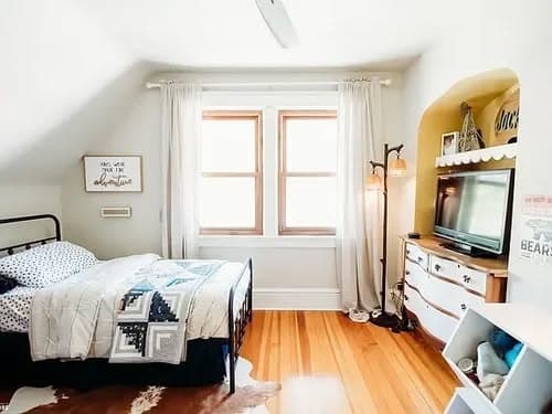 Cozy bedroom with a black metal bed frame, large windows, and wooden flooring.