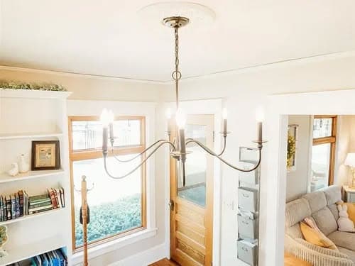 Modern chandelier in bright living room with bookshelf and cozy seating area.