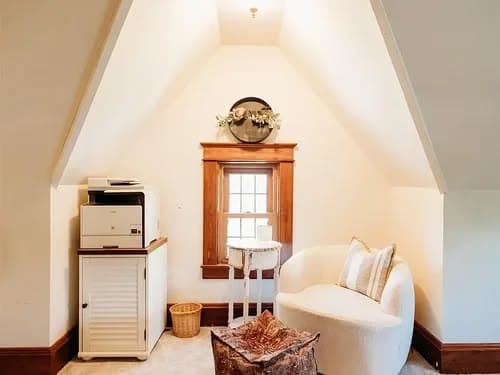 Cozy attic space with a white chair, printer, and decorative window. Ideal for relaxation.