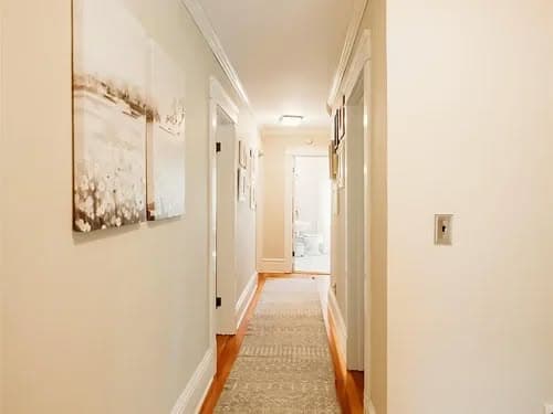 Bright hallway with artwork, leading to a bathroom at the end, featuring warm wooden floors.