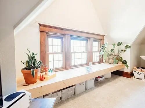 Cozy attic space with large windows, plants, and a wooden bench for storage.