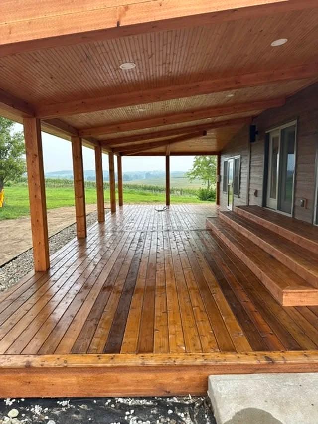 Spacious wooden deck with covered seating area overlooking green landscape.