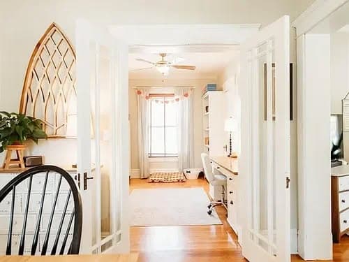 Bright home office with white desks, decorative plants, and an open doorway. Ideal workspace design.