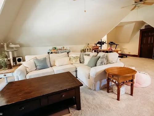 Cozy attic living room with sectional couch, coffee table, and cat tree under sloped ceiling.