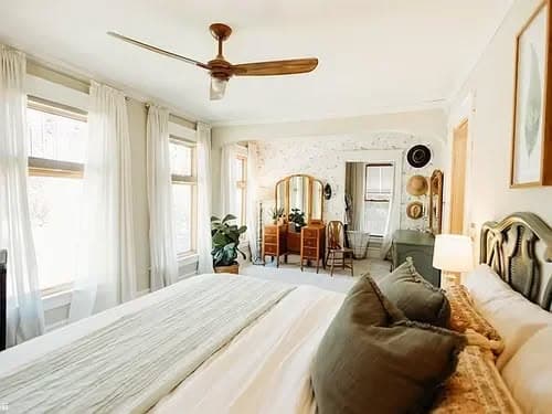 Bright, serene bedroom with a ceiling fan, large windows, and elegant decor elements.