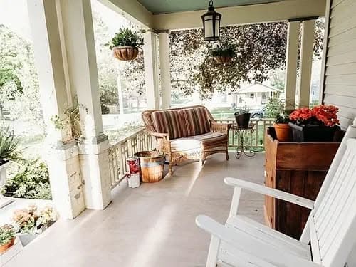 Cozy porch with wicker furniture, potted plants, and vibrant flowers in a sunny setting.