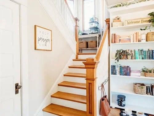 Bright and inviting hallway featuring wooden stairs, bookshelves, and a welcoming decor sign.