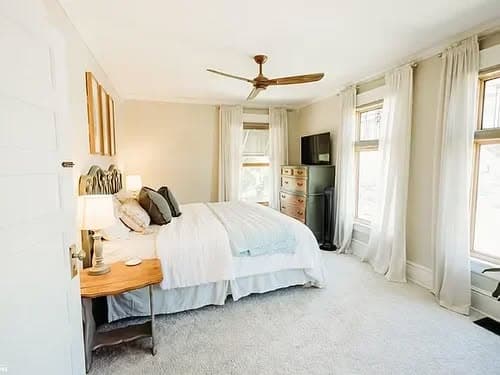 Bright, serene bedroom with a king bed, ceiling fan, and large windows for natural light.