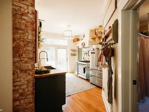 Modern kitchen with a brick wall, stainless steel appliances, and natural light. Cozy home vibe.