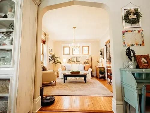 Cozy living room with white sofa, wooden flooring, and natural light through large windows.