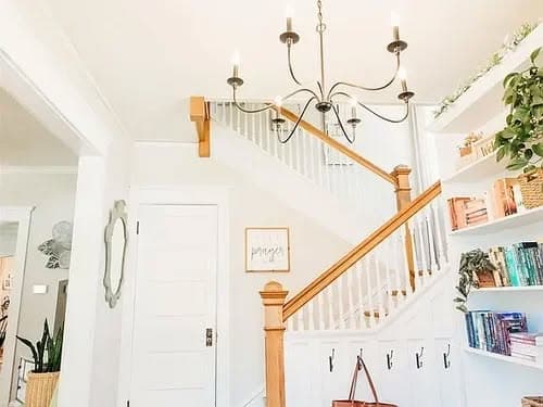 Bright entryway showcasing a staircase, chandelier, and built-in bookshelves with greenery.