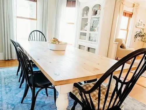 Bright dining room with wooden table, black chairs, and a bowl of fruit centerpiece.