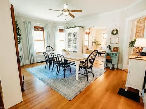 Bright dining room with a white table, black chairs, and hardwood floors, featuring natural light.