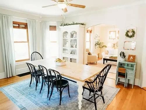 Bright dining room featuring a large wooden table with black chairs, natural light, and elegant decor.