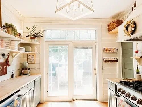 Bright modern kitchen with open shelves, natural light, and sliding glass door leading outdoors.