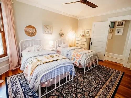 Cozy twin bedroom with white metal beds, pastel decor, and a patterned area rug.