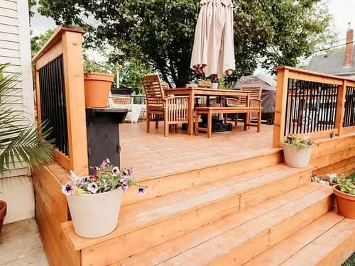 Cozy wooden deck with dining set, potted flowers, and patio umbrella. Ideal outdoor space.