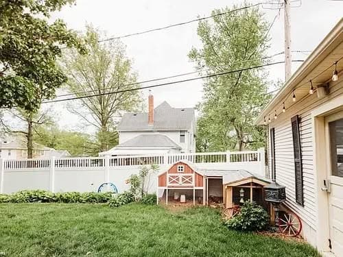 Backyard scene featuring a playhouse, fence, and greenery with trees and a house in the background.