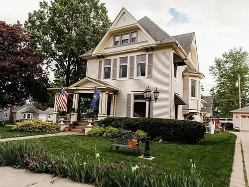 Victorian-style house with flags, manicured lawn, and decorative garden in front.