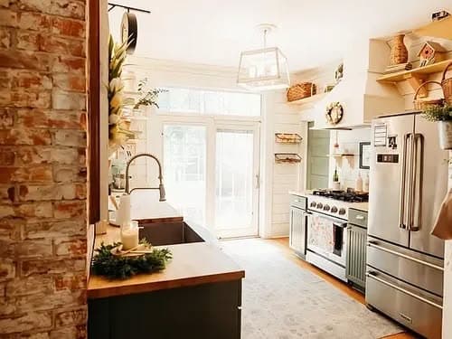 Bright kitchen with modern appliances, rustic brick wall, and natural light from large windows.