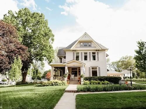 Charming two-story Victorian house with a porch, surrounded by lush green gardens.