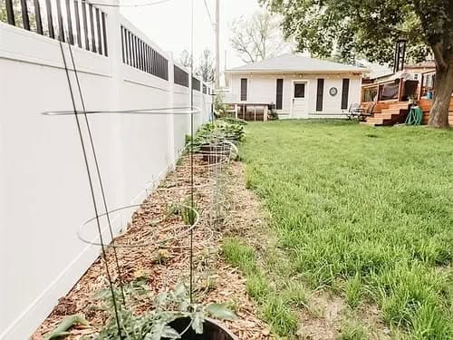 Backyard garden with trellises and a white fence, featuring a house and lush green lawn.