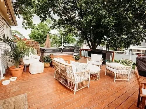 Cozy outdoor living space with wicker furniture, potted plants, and a hot tub on wooden deck.