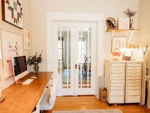 Cozy home office with a wooden desk, computer, and glass French doors leading to a bright room.