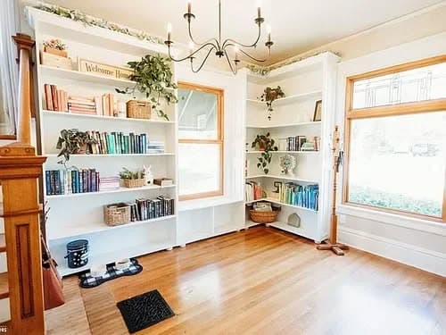 Cozy reading nook with bookshelves, chandelier, and natural light from large windows.