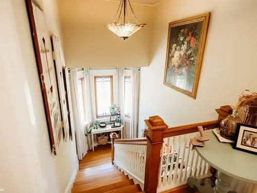 View of a well-lit staircase with wooden railing, artwork, and a bright window nook.