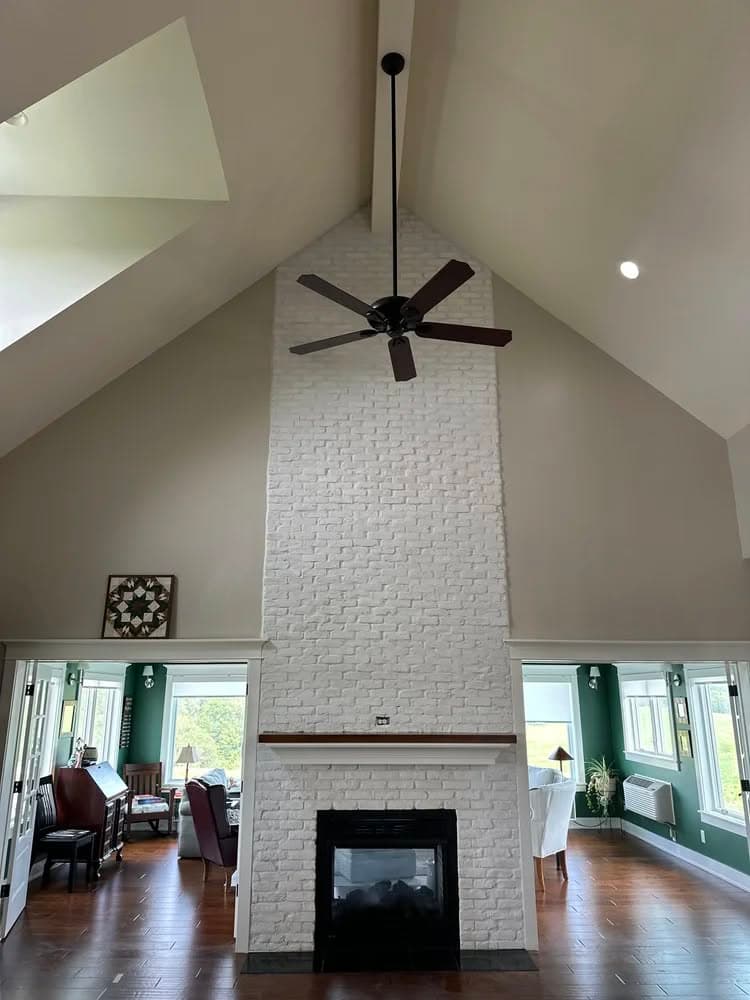 Modern living room with high ceilings, white brick fireplace, and stylish ceiling fan.
