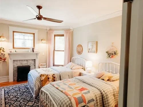 Cozy bedroom with two twin beds, decorative quilts, and a charming fireplace.