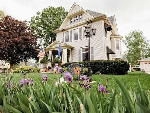 Victorian house with American flags and purple irises in the garden, showcasing classic architecture.