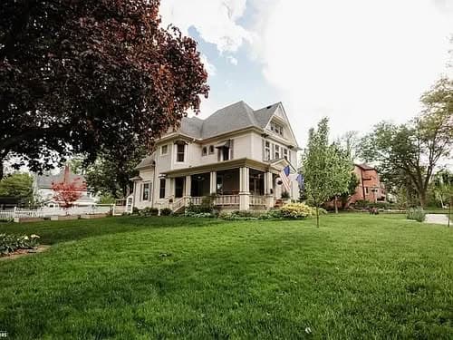Victorian-style house with a well-manicured lawn and colorful trees under a bright sky.