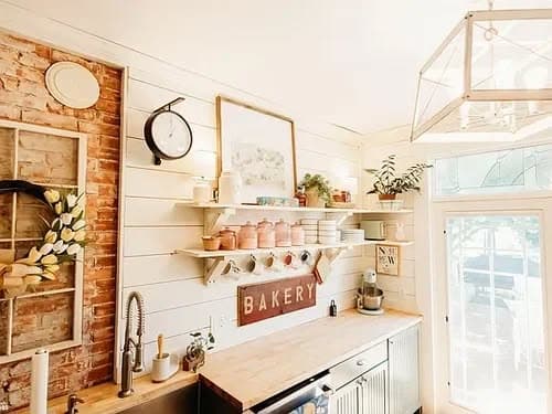 Cozy kitchen with rustic decor, bakery sign, shelves, and plants, featuring modern appliances.