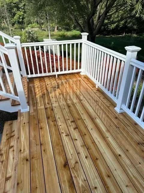Newly built wooden deck with white railings, surrounded by greenery and trees.