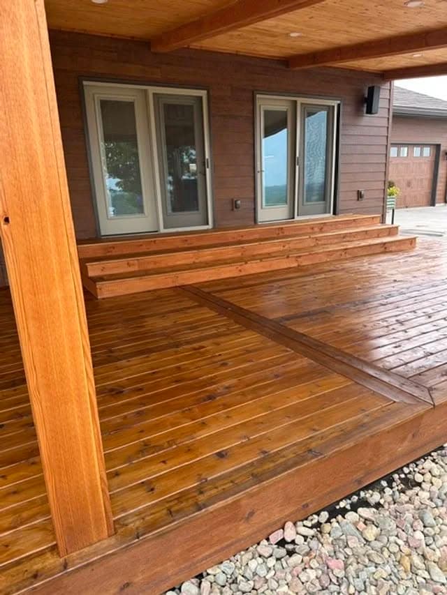 Modern wooden deck with freshly stained planks and large glass doors leading to a home.