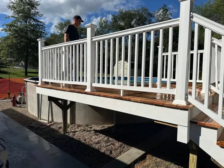 Man walking on a wooden deck with white railings above an above-ground pool.