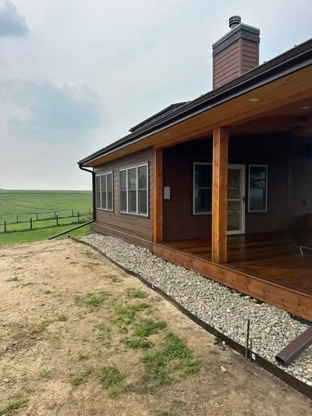 Modern wooden house with spacious porch, surrounded by green grass and open field.