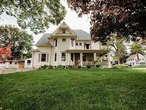 Victorian-style house with lush green lawn and trees, showcasing charming architectural details.