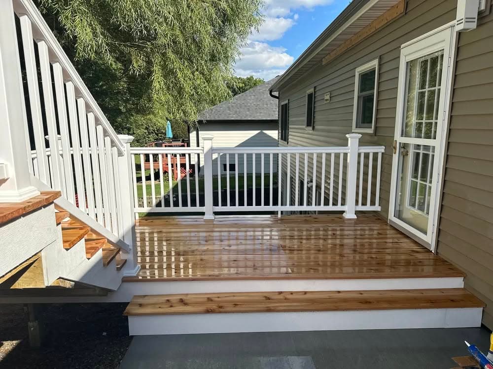 Newly built wooden deck with white railing and stairs, featuring a smooth finish and sunny sky.