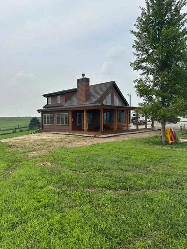 Modern farmhouse with a spacious porch, surrounded by lush green grass and open fields.