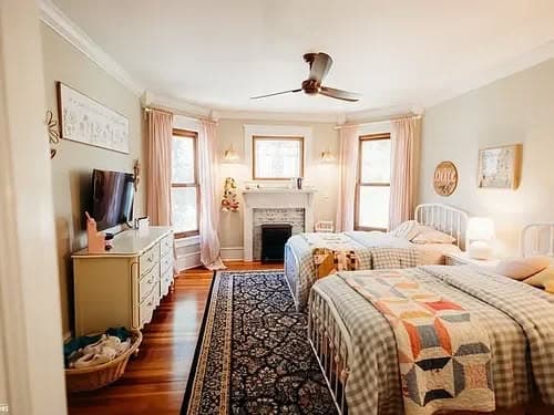 Cozy bedroom with two beds, fireplace, and a decorative rug in natural light.