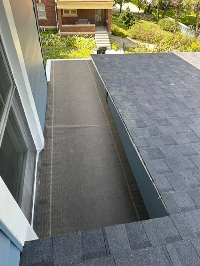Flat roofing section featuring asphalt shingles and a clear view of a residential area.