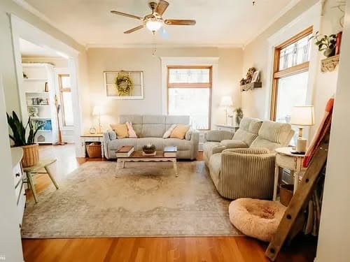 Cozy living room with gray sofas, wooden coffee table, and soft area rug, featuring natural light.