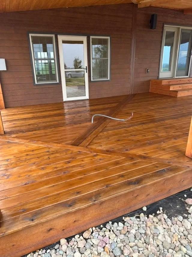 Clean wooden deck of a house with a door, featuring a hose and rocky landscaping.