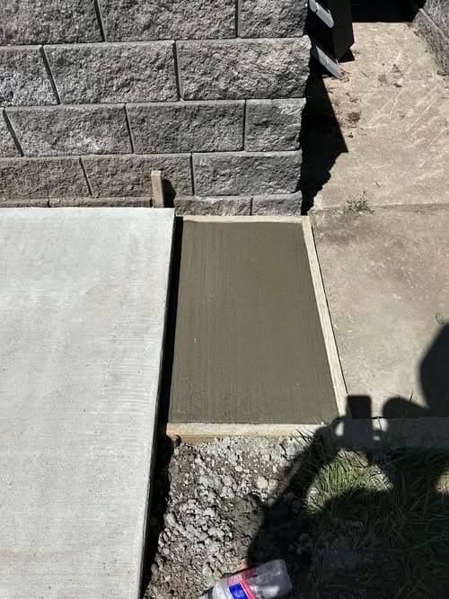 Freshly poured concrete slab next to a stone wall and a concrete sidewalk.